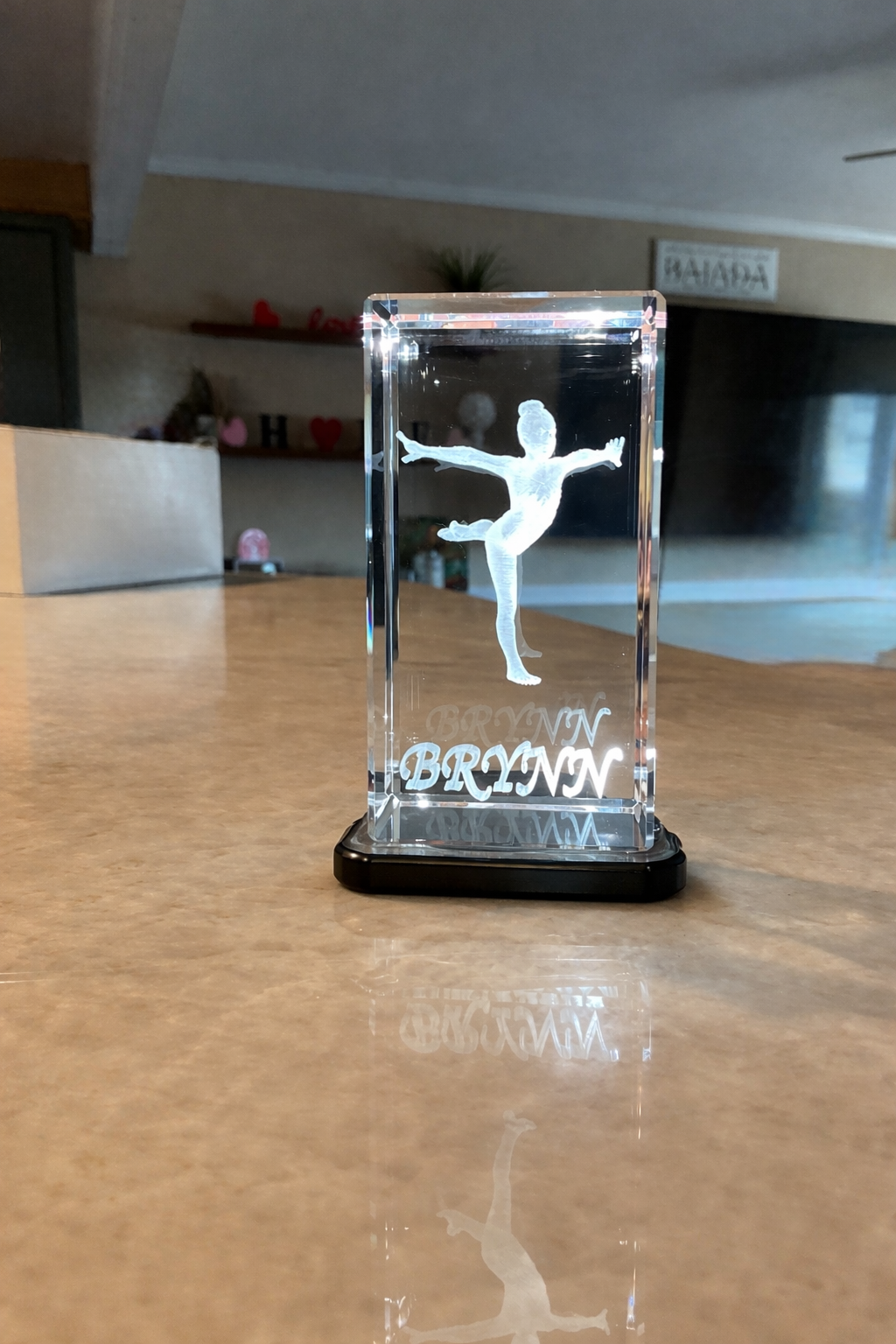 Crystal block with a gymnast silhouette and engraved name on a wooden surface.