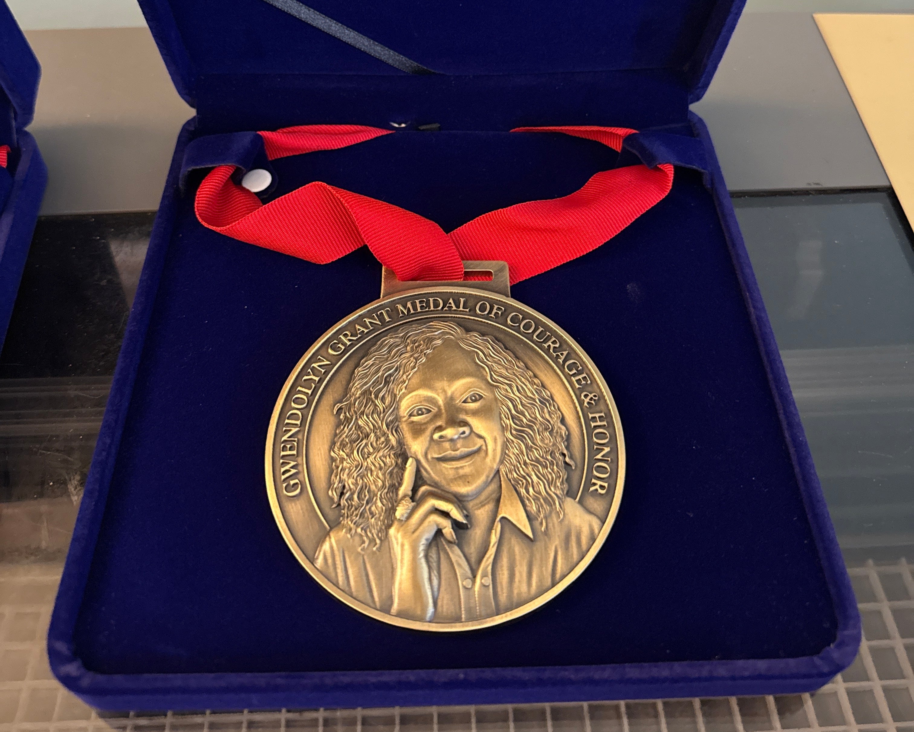 Gold medal with red ribbon in a blue case on a tiled wall background