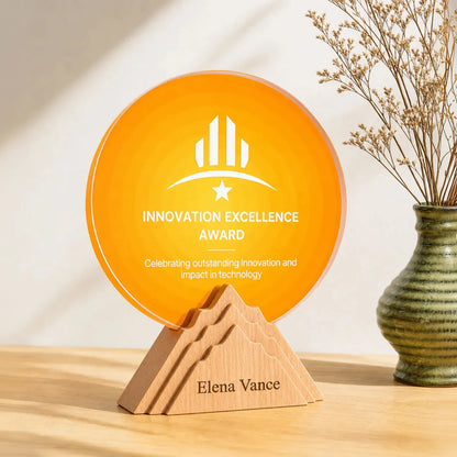 Orange round crystal award engraved with a logo and award title, set in a stepped beechwood mountain base engraved with the recipient's name