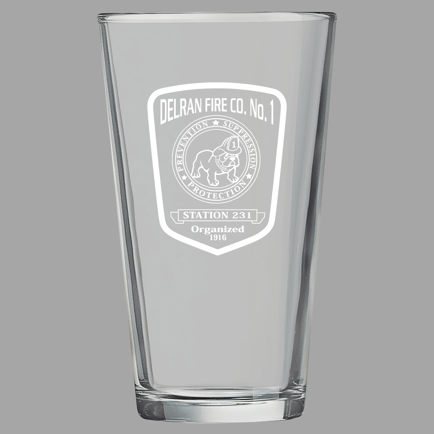 Clear glass pint glass with engraved logo on a gray background