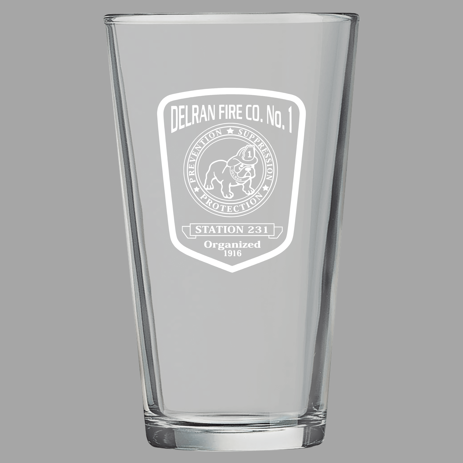 Clear glass pint glass with engraved logo on a gray background